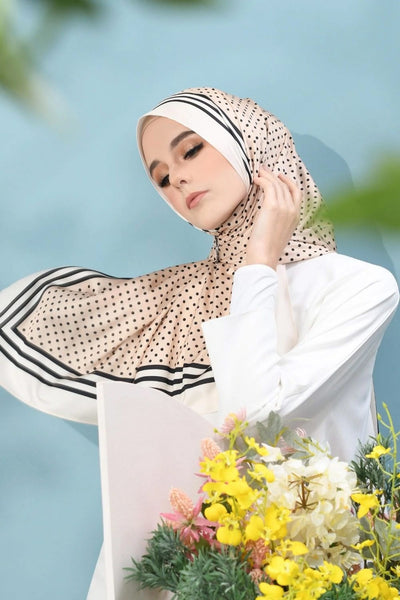 A woman in a sophisticated beige chiffon hijab dotted with black, bordered with stripes, exuding elegance and modesty, perfect for versatile styling