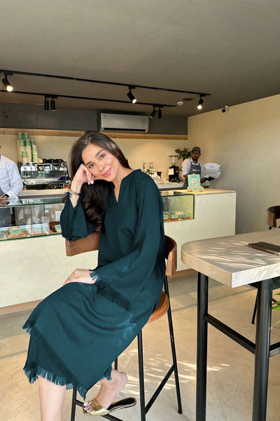 Woman in a teal dress sitting at a cafe counter with a blurred background