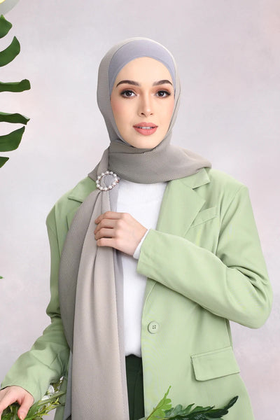 Stylish woman wearing a sophisticated gray Scarf with a delicate brooch exemplifying modern modest fashion.