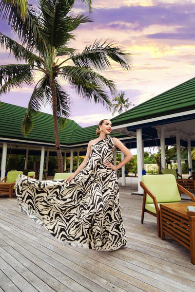 Elegant woman in one shoulder Zephyr Zebra Whisper Kaftan with a tropical backdrop, embodying resort luxury and style